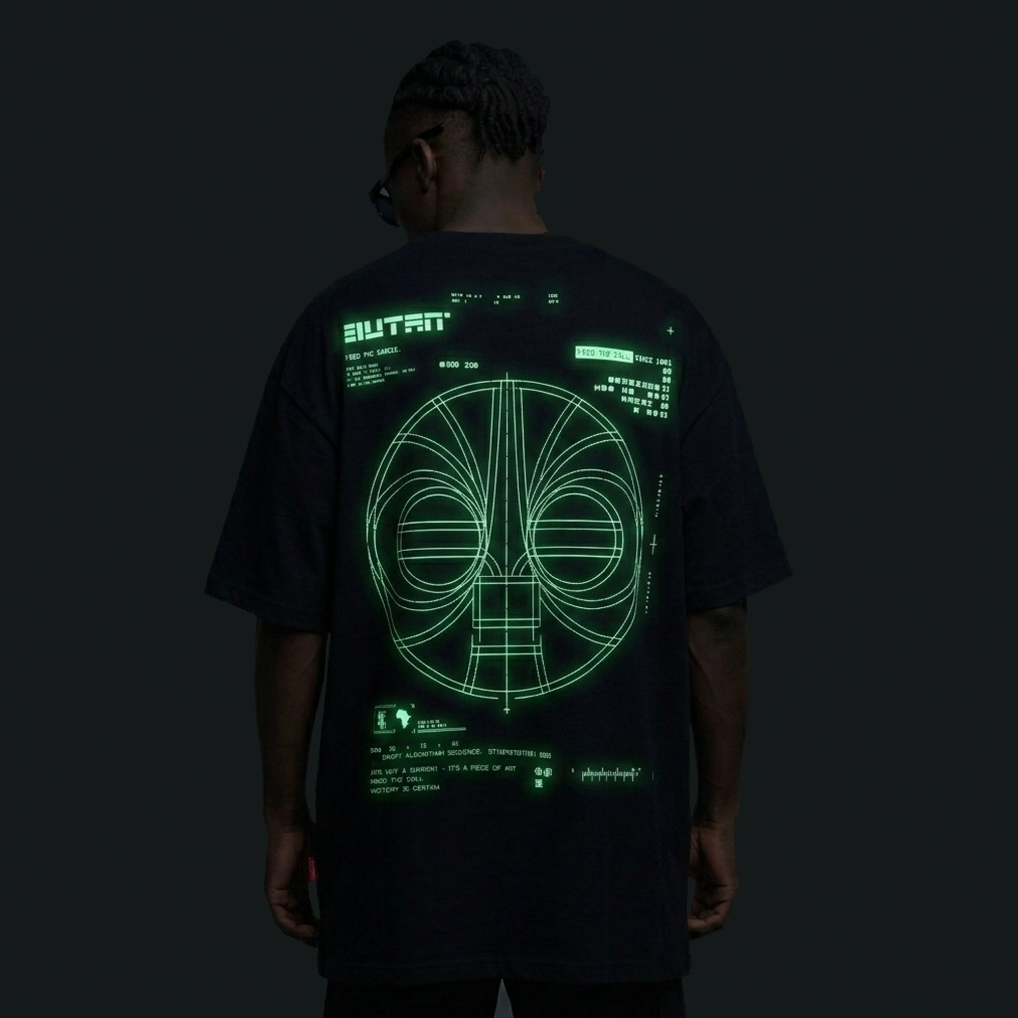 Person wearing a black t-shirt with green technical design on the back against a dark background