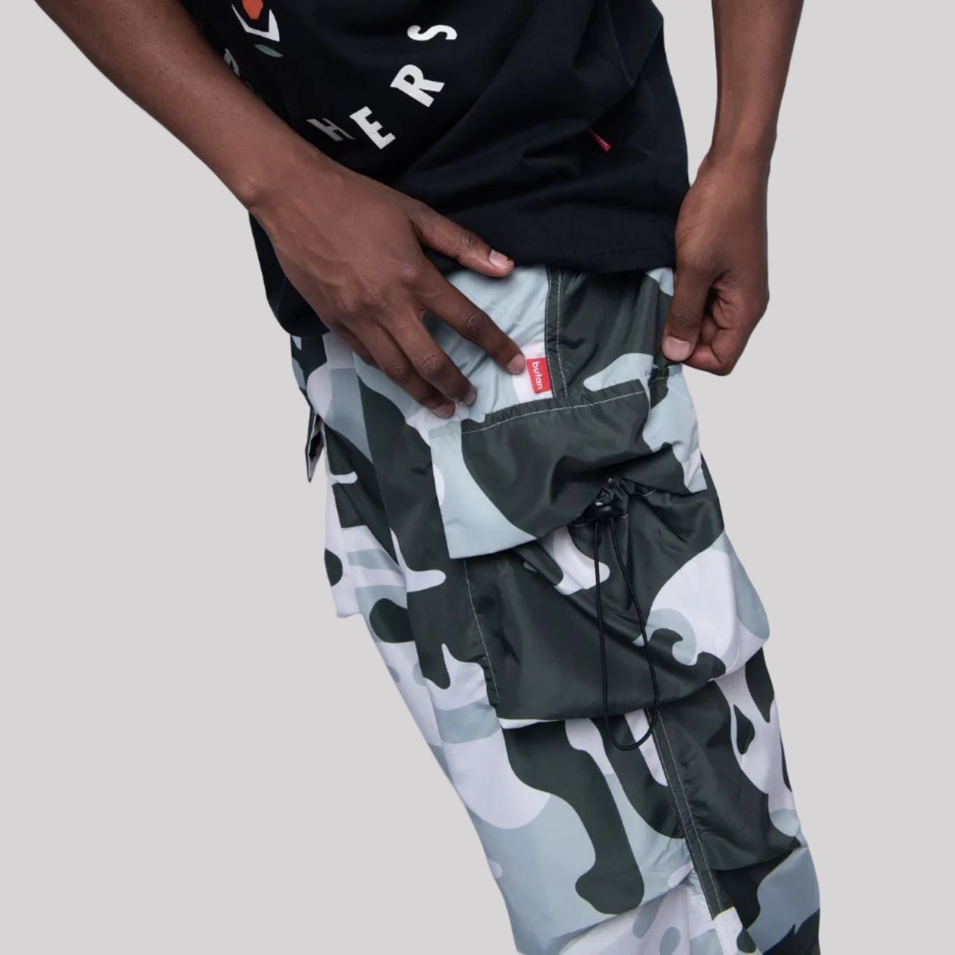 Person wearing a black t-shirt with a graphic design and camouflage pants on a white background