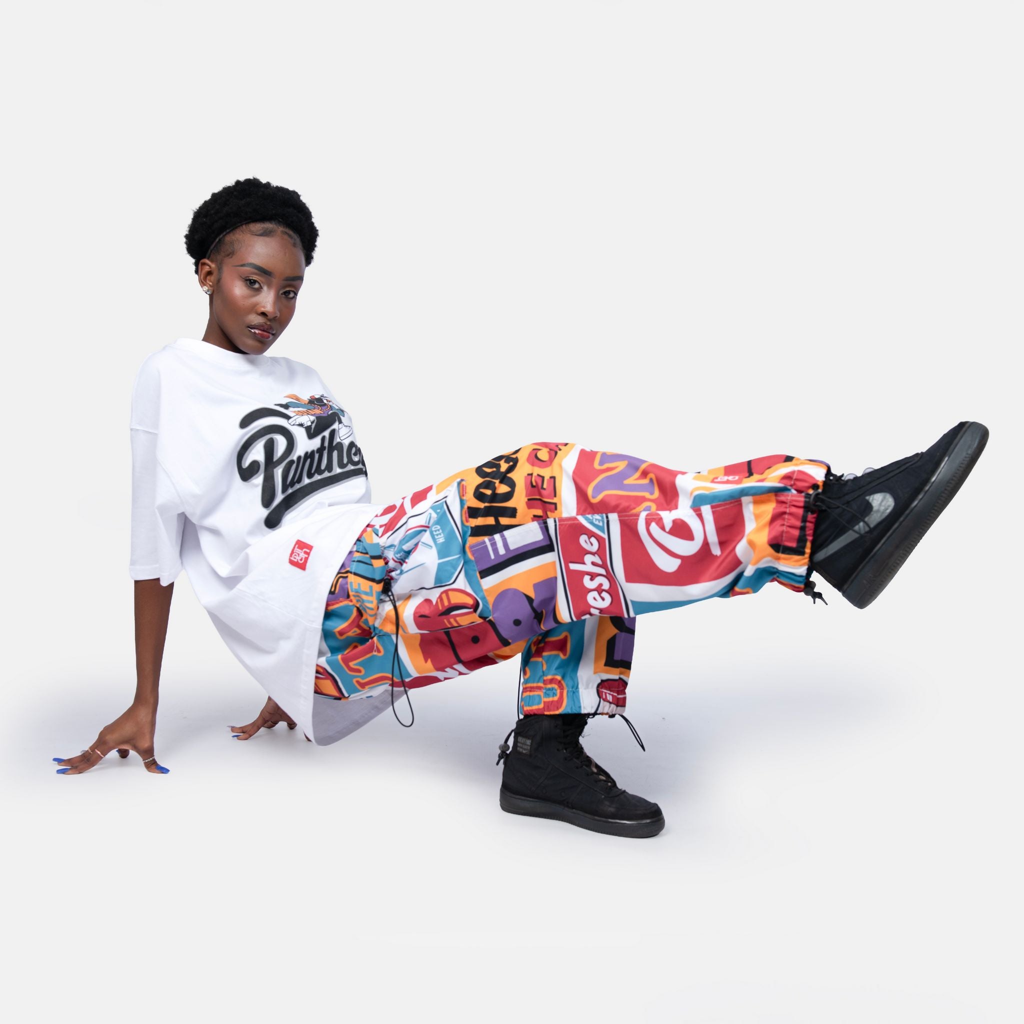 Person wearing a white t-shirt with a logo and colorful pants on a white background