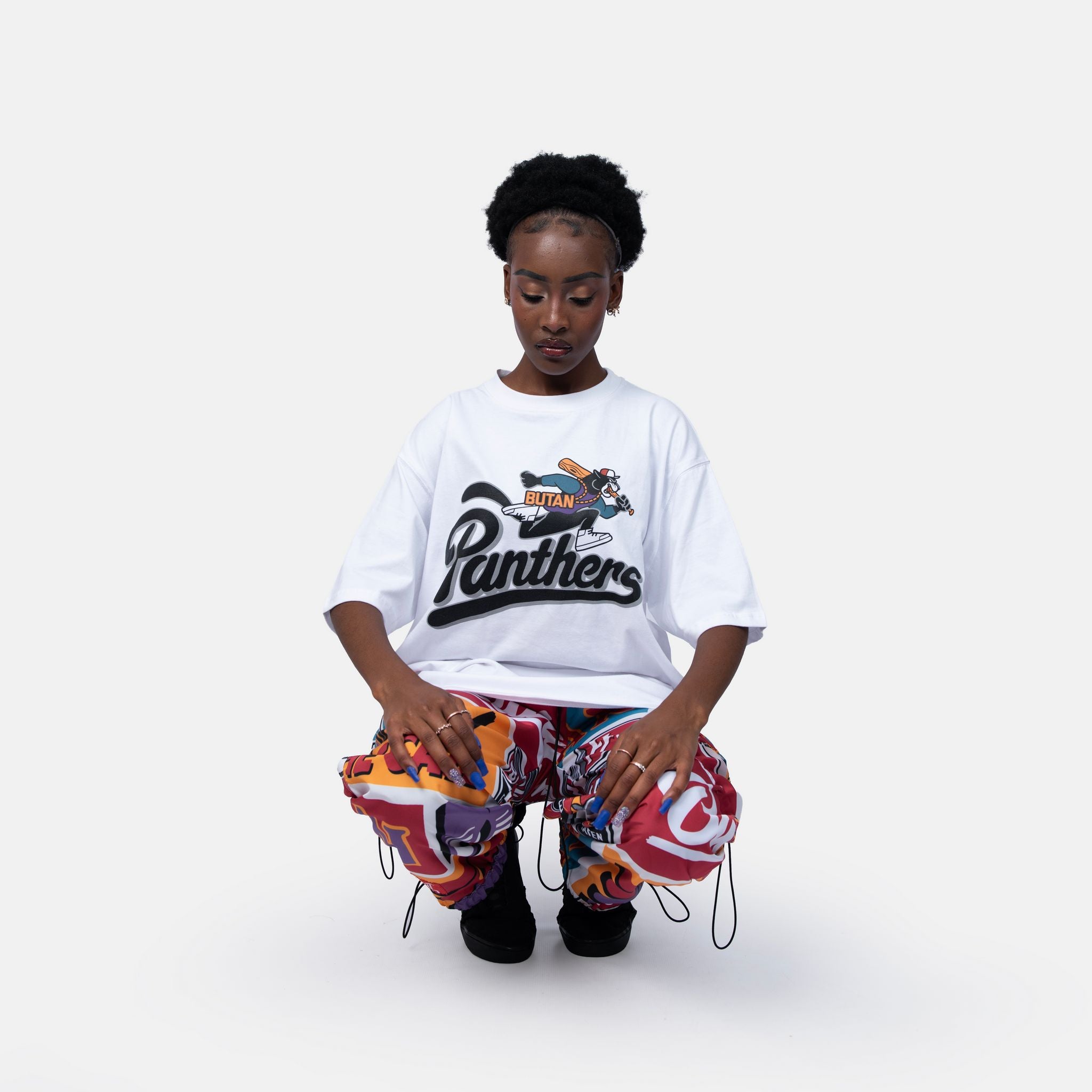 Person wearing a white t-shirt with a 'Panthers' logo and colorful pants on a white background