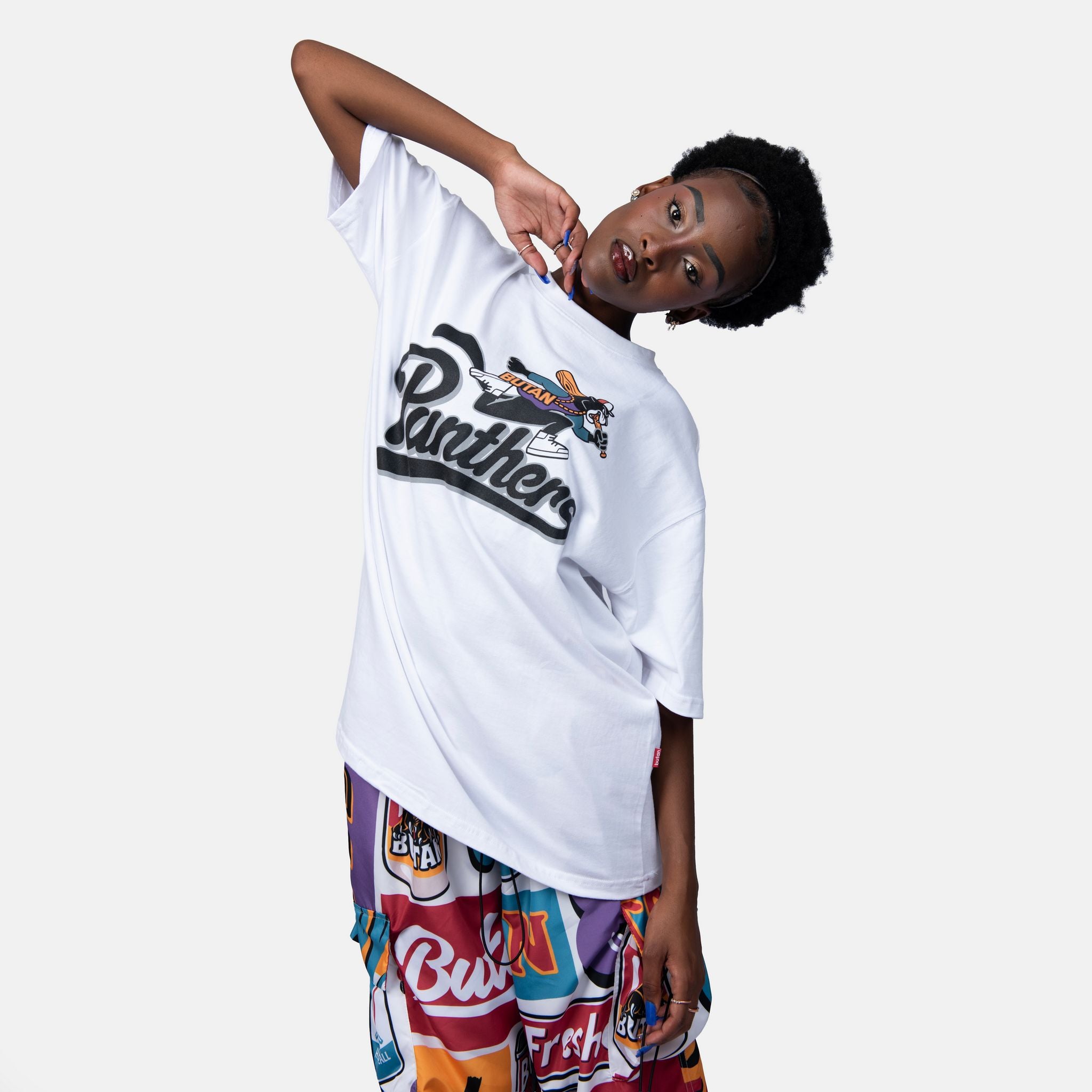 Person wearing a white t-shirt with a logo and colorful pants on a white background