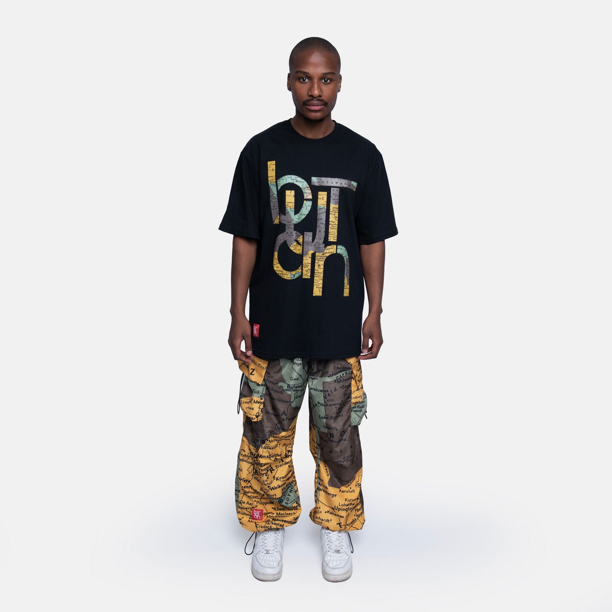 Person wearing a black t-shirt with colorful text and patterned pants on a white background