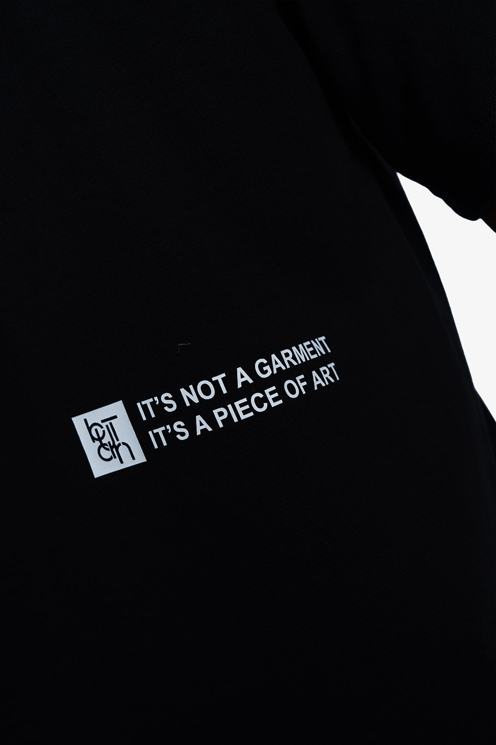 Close-up of a black garment featuring a white printed logo and the text 'IT'S NOT A GARMENT IT'S A PIECE OF ART' on the chest.