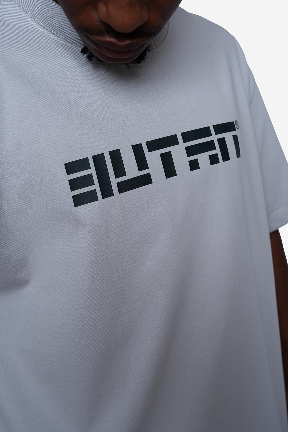 A close-up of a person wearing a white t-shirt with a bold black geometric logo across the chest.
