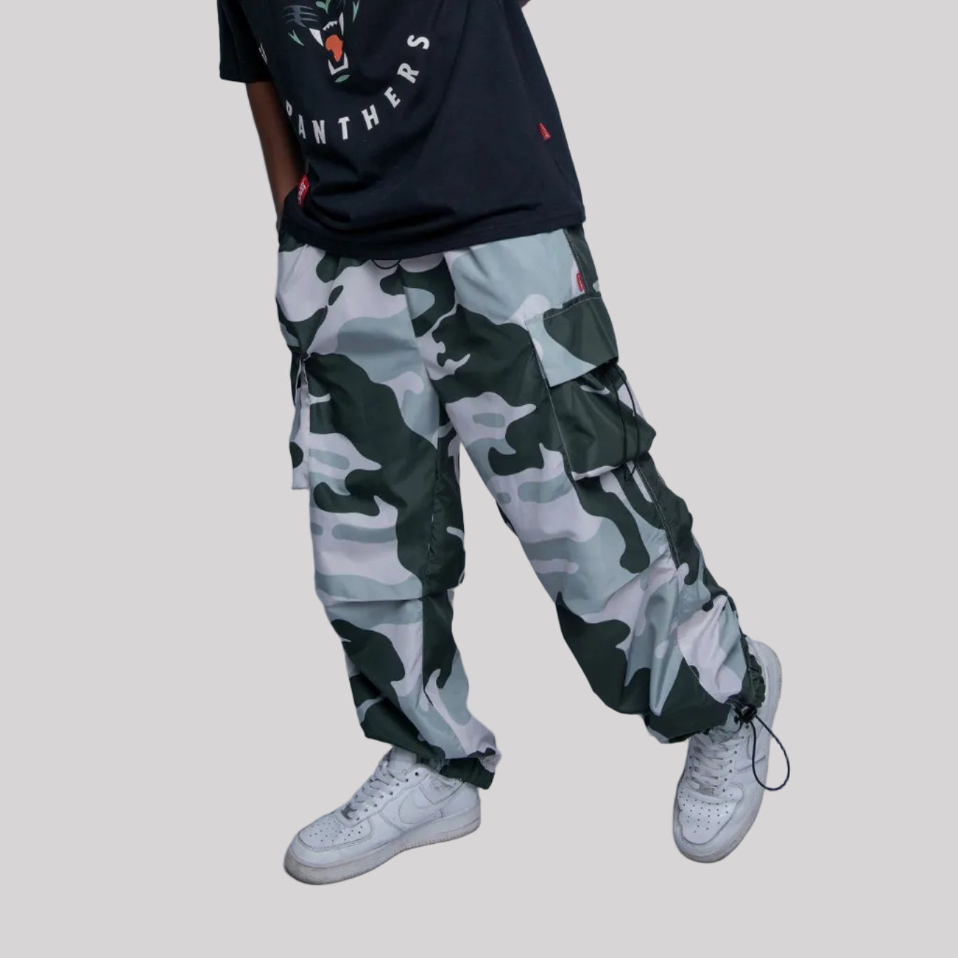 Person wearing a black t-shirt with graphics and camouflage pants on a plain background