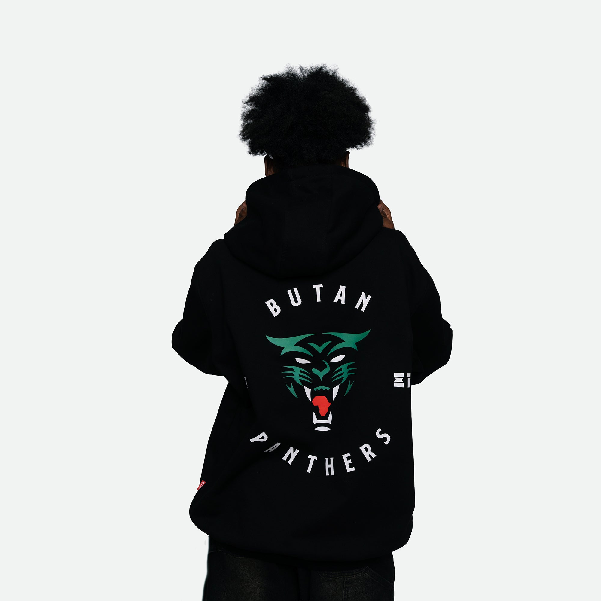 A person viewed from behind wearing a black hoodie with a large graphic on the back. The design features a green and white panther face with red details, surrounded by the text 'BUTAN PANTHERS' in white.