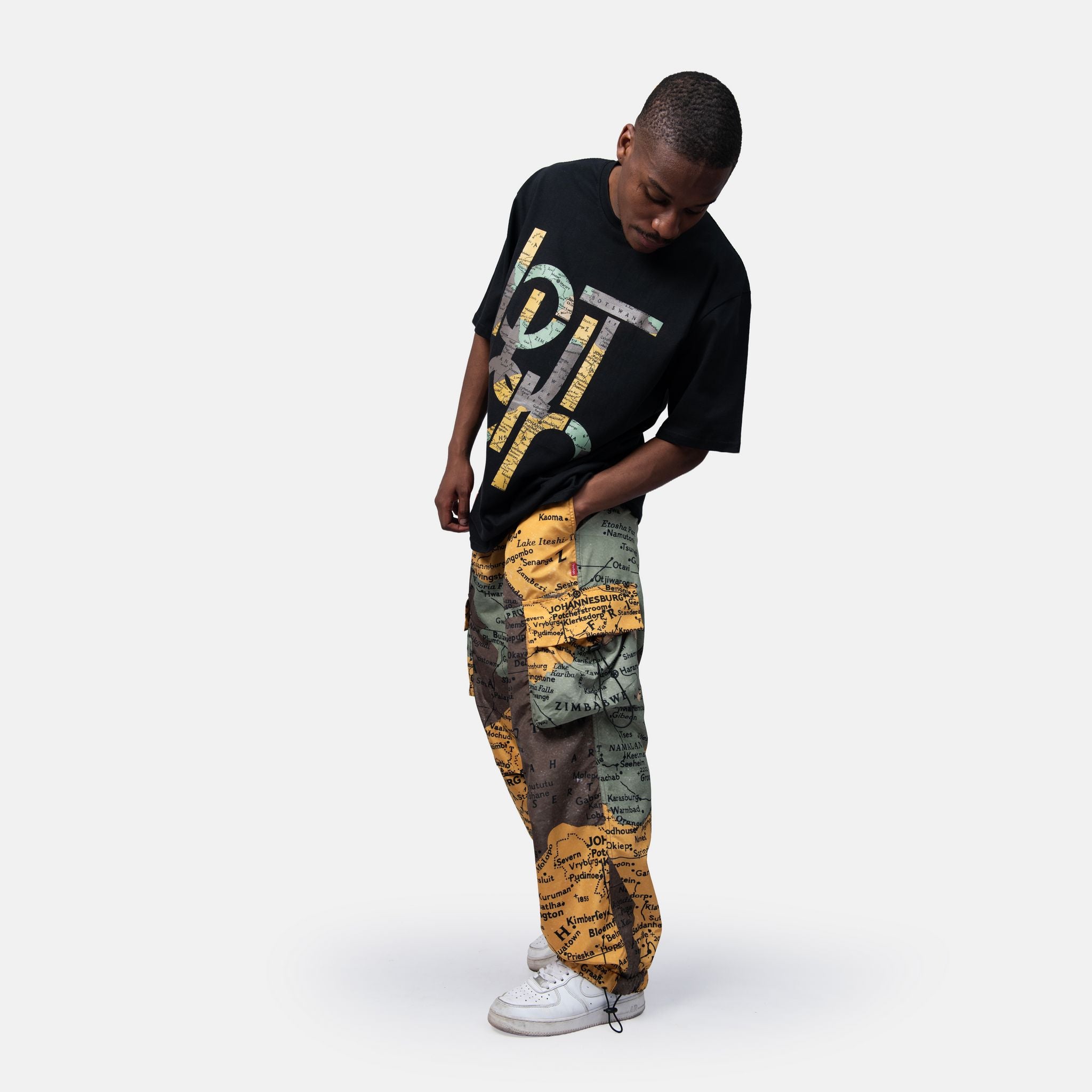 Person wearing a black sweater with colorful text and patterned pants on a white background