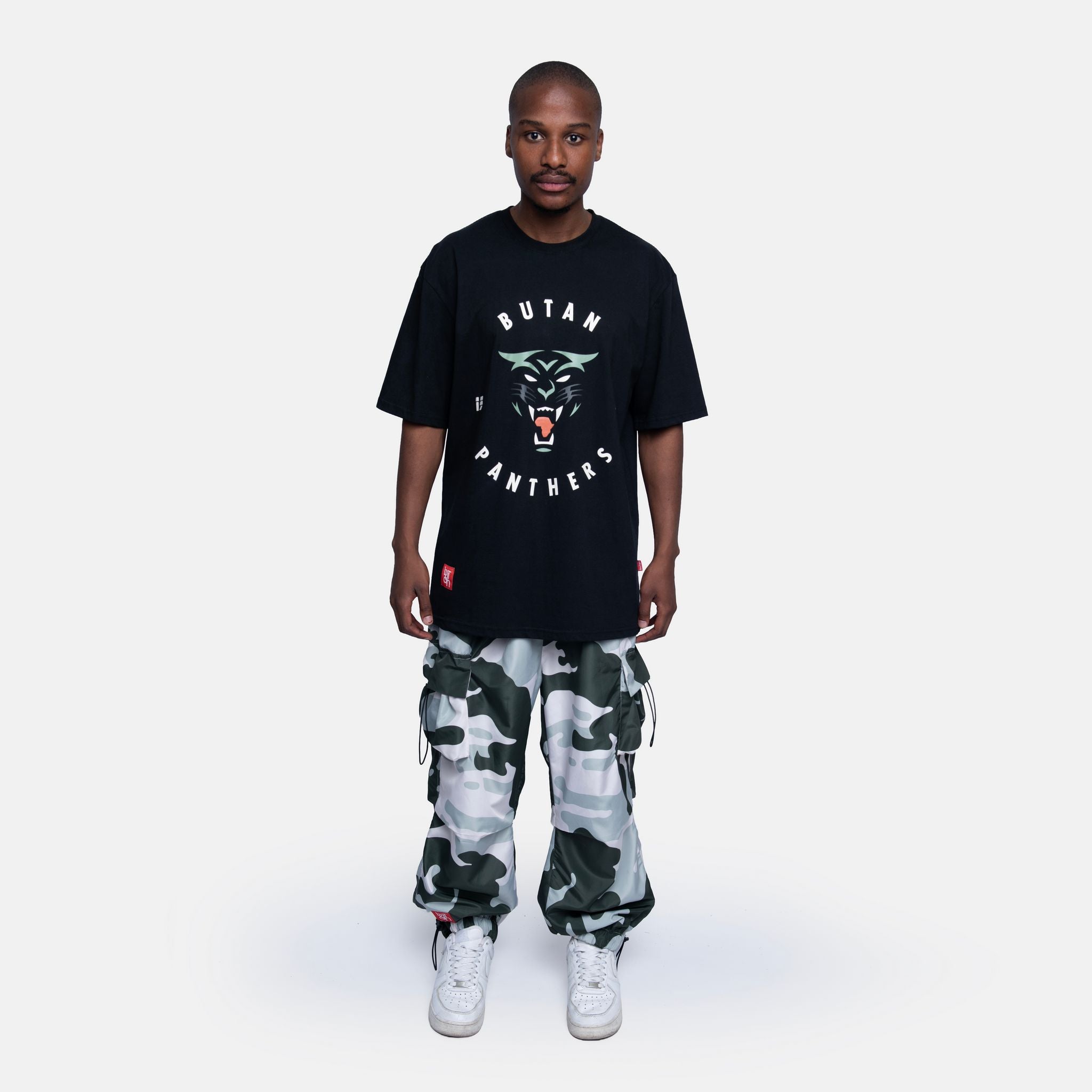 Person wearing a black 'Butan Panthers' t-shirt and camouflage pants on a white background