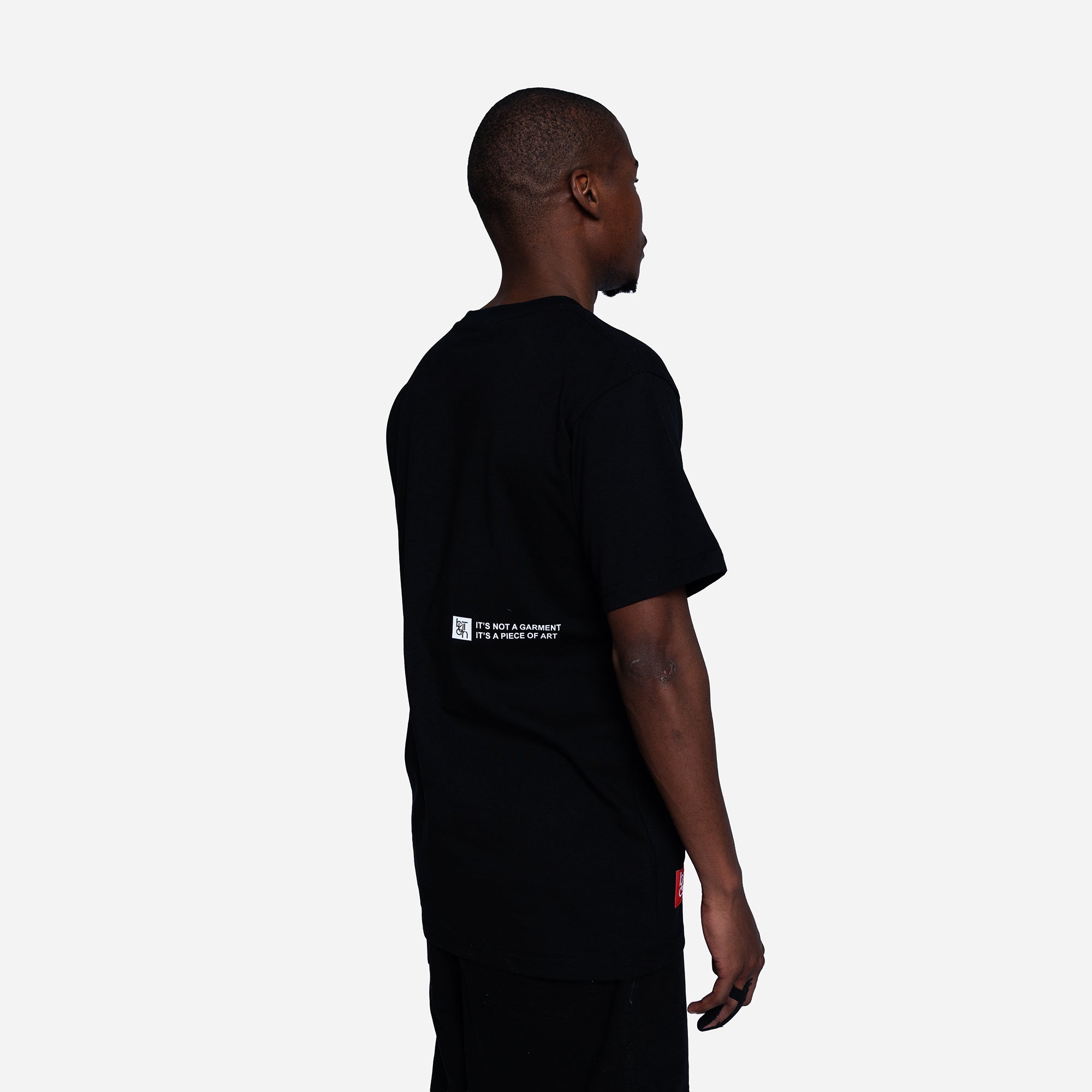 A man shown from the back wearing a black short-sleeve t-shirt with a small white graphic text print on the left side of the back, set against a plain light gray background.