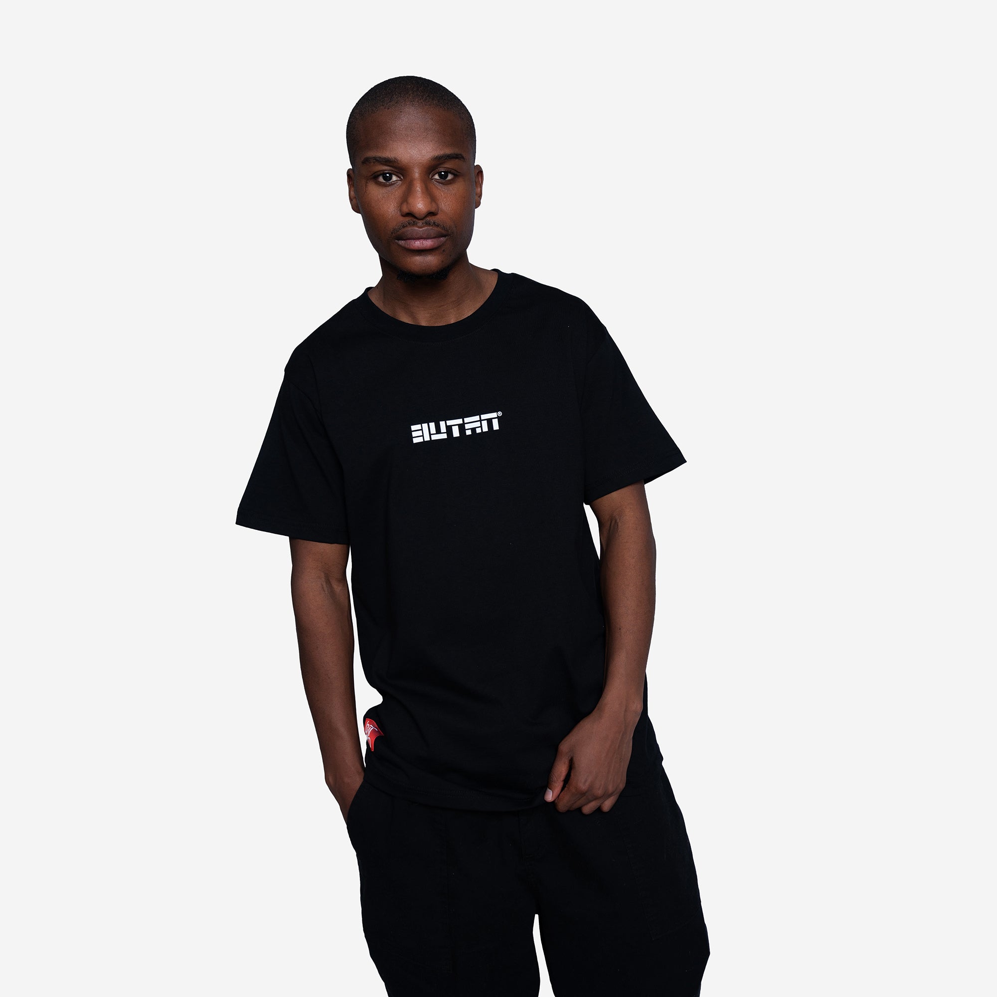 A man wearing a black crewneck t-shirt with the word 'BUTAN' printed in white across the chest, paired with black sweatpants, set against a plain light gray background.