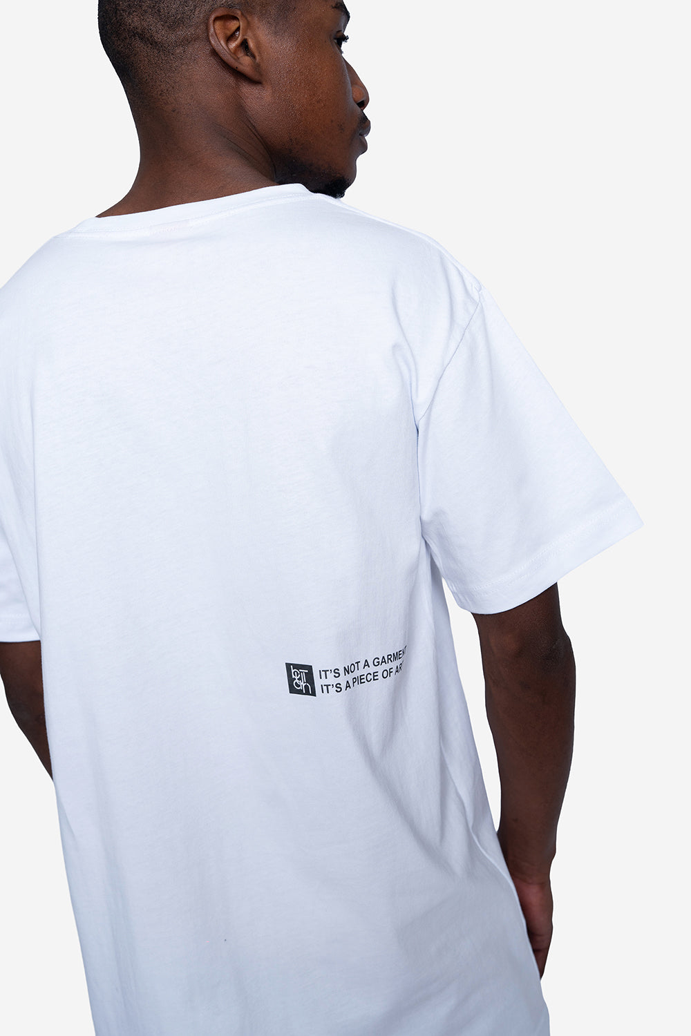 A man wearing a white short-sleeve t-shirt, shown from the back. The shirt features a small black graphic and text printed on the lower left side.