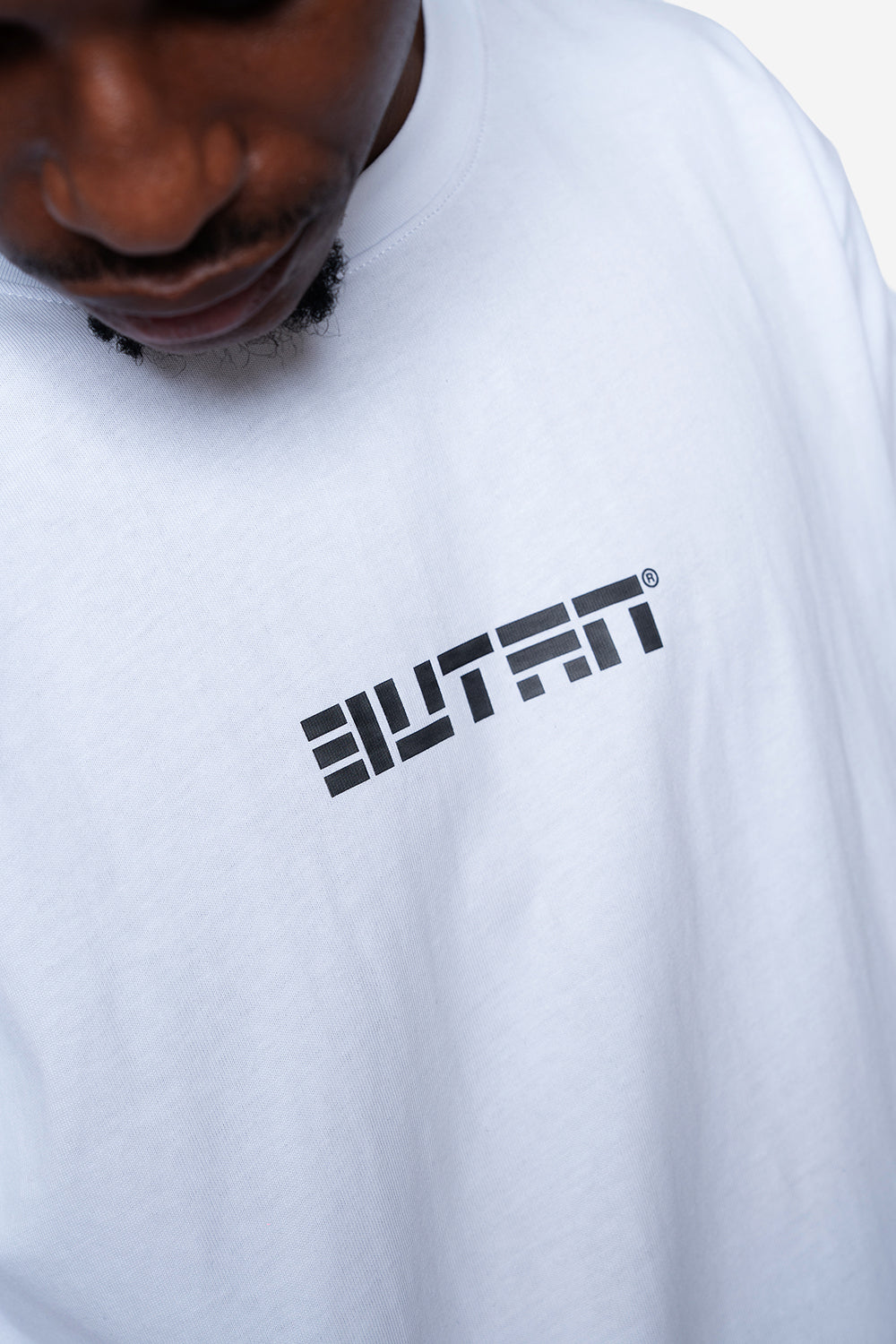 A close-up of a person wearing a white crewneck t-shirt with a black stylized 'BUTAN' logo printed on the chest.