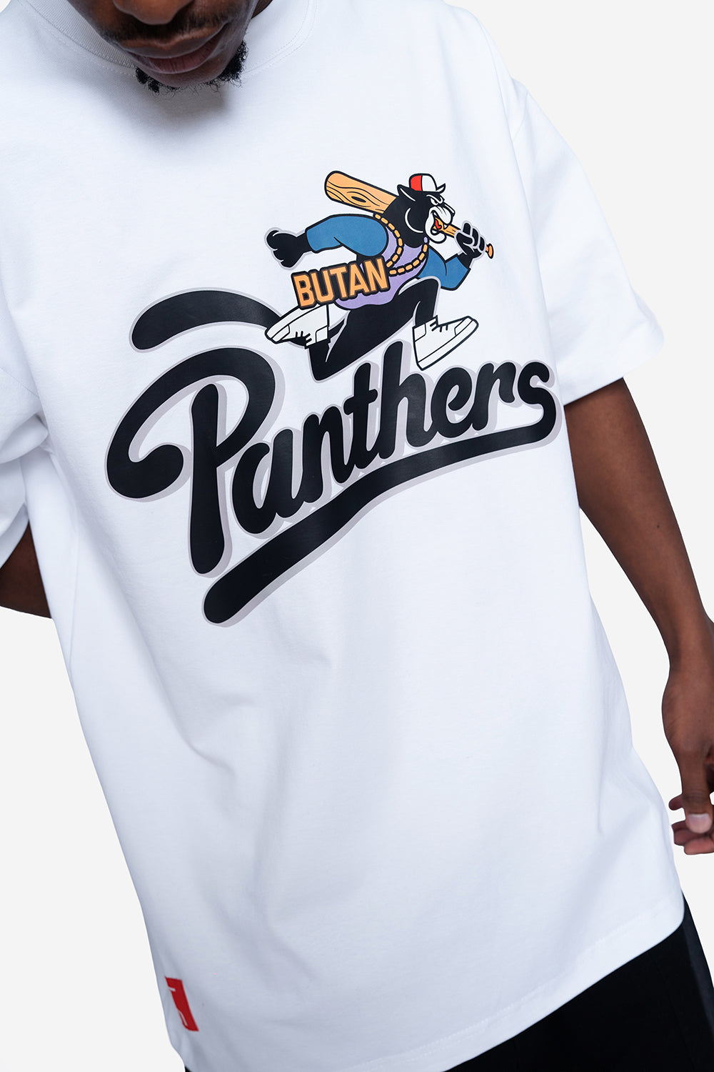 A close-up of a person wearing a white t-shirt with a large graphic print. The graphic features the word 'Panthers' in a bold black script, with a cartoon character labeled 'Butan' playing baseball above it.