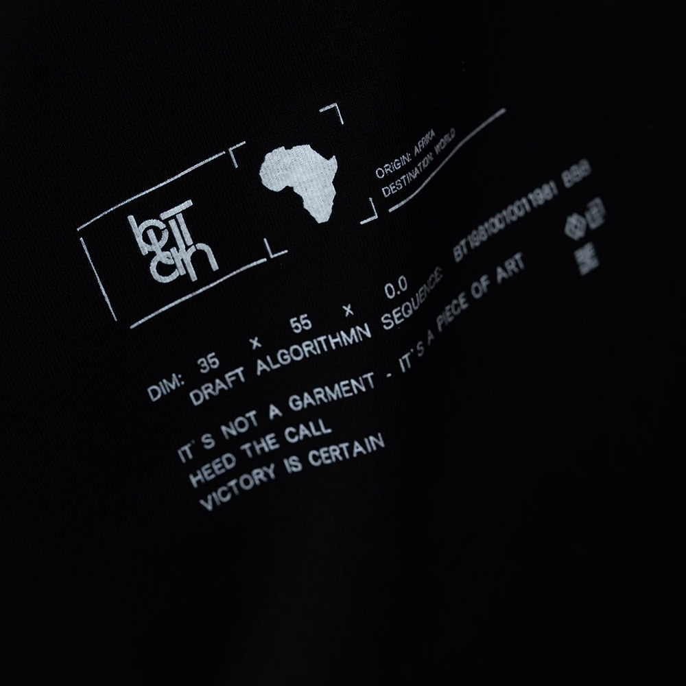 Close-up of a black garment featuring white graphic text and a small white silhouette of Africa, with additional white printed design elements on a dark background.