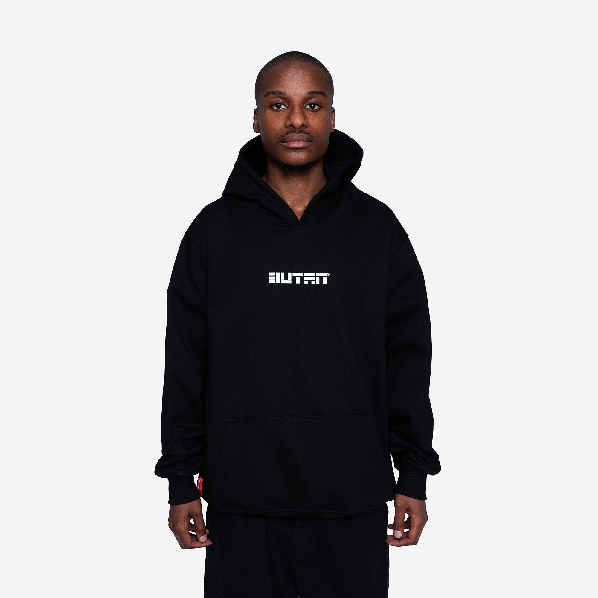 A man wearing a black pullover hoodie with the word 'BUTAN' printed in white block letters across the chest, standing against a light gray background.