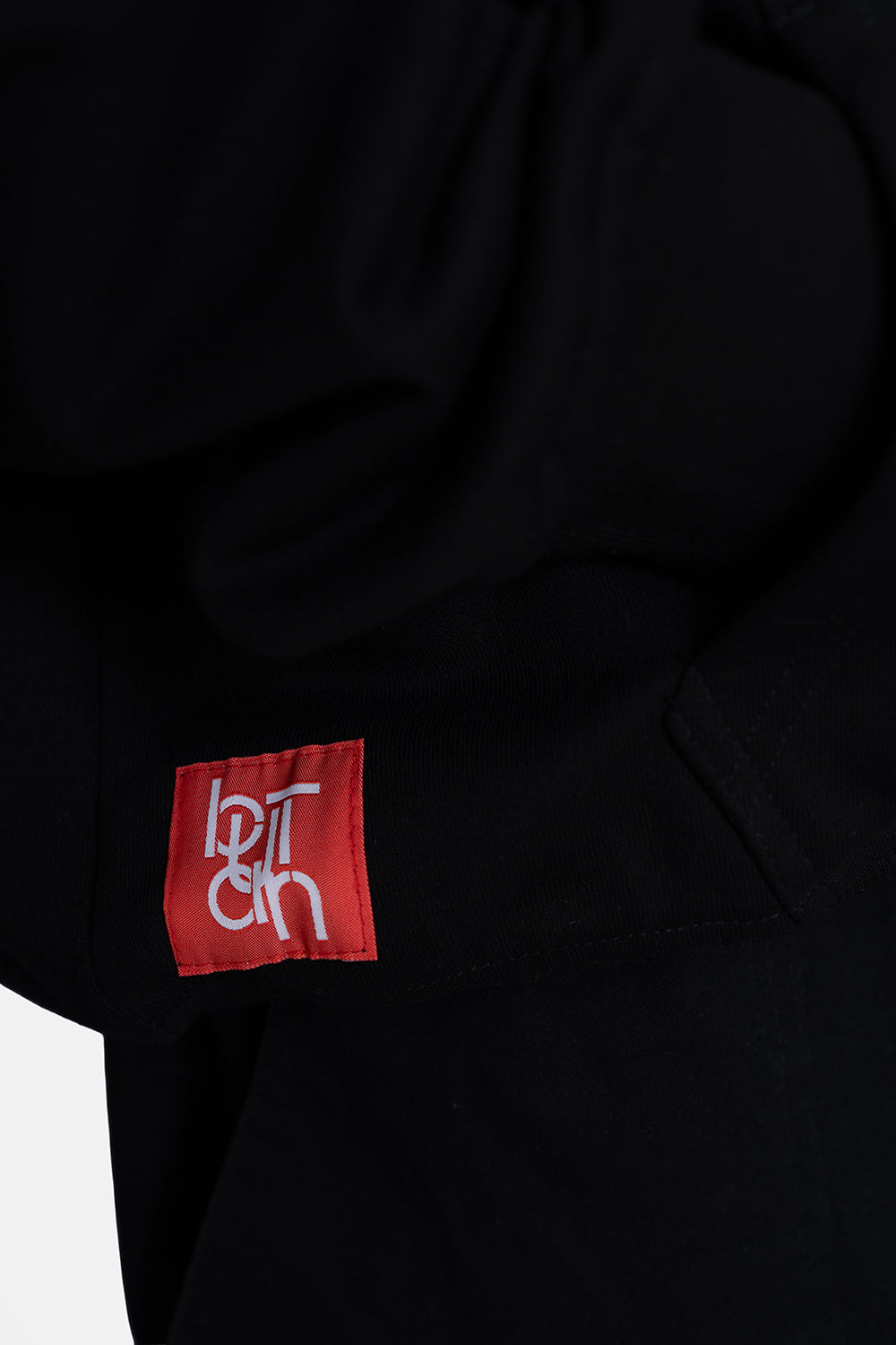 Close-up of a black garment featuring a red square patch with white stylized text on the side.