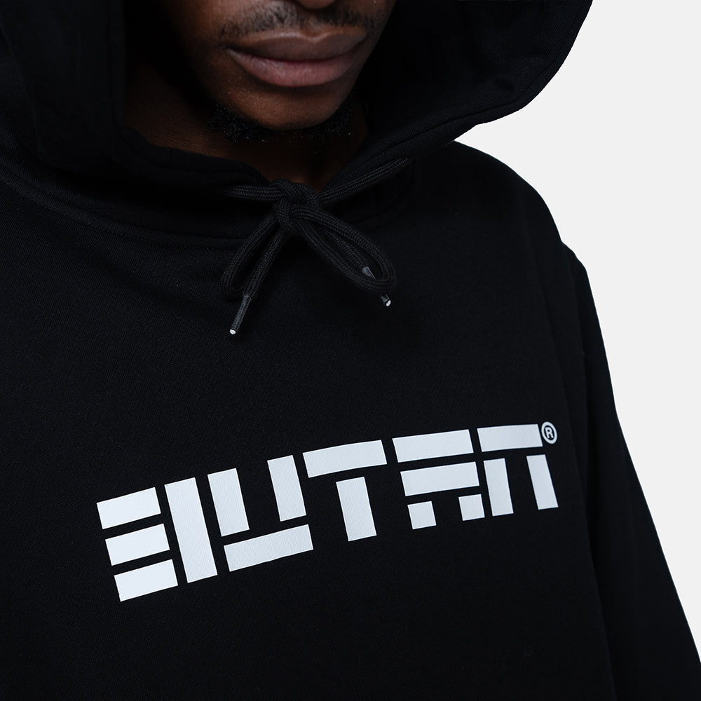 A close-up of a person wearing a black pullover hoodie with a bold white geometric logo across the chest. The logo reads 'BUTEN'.